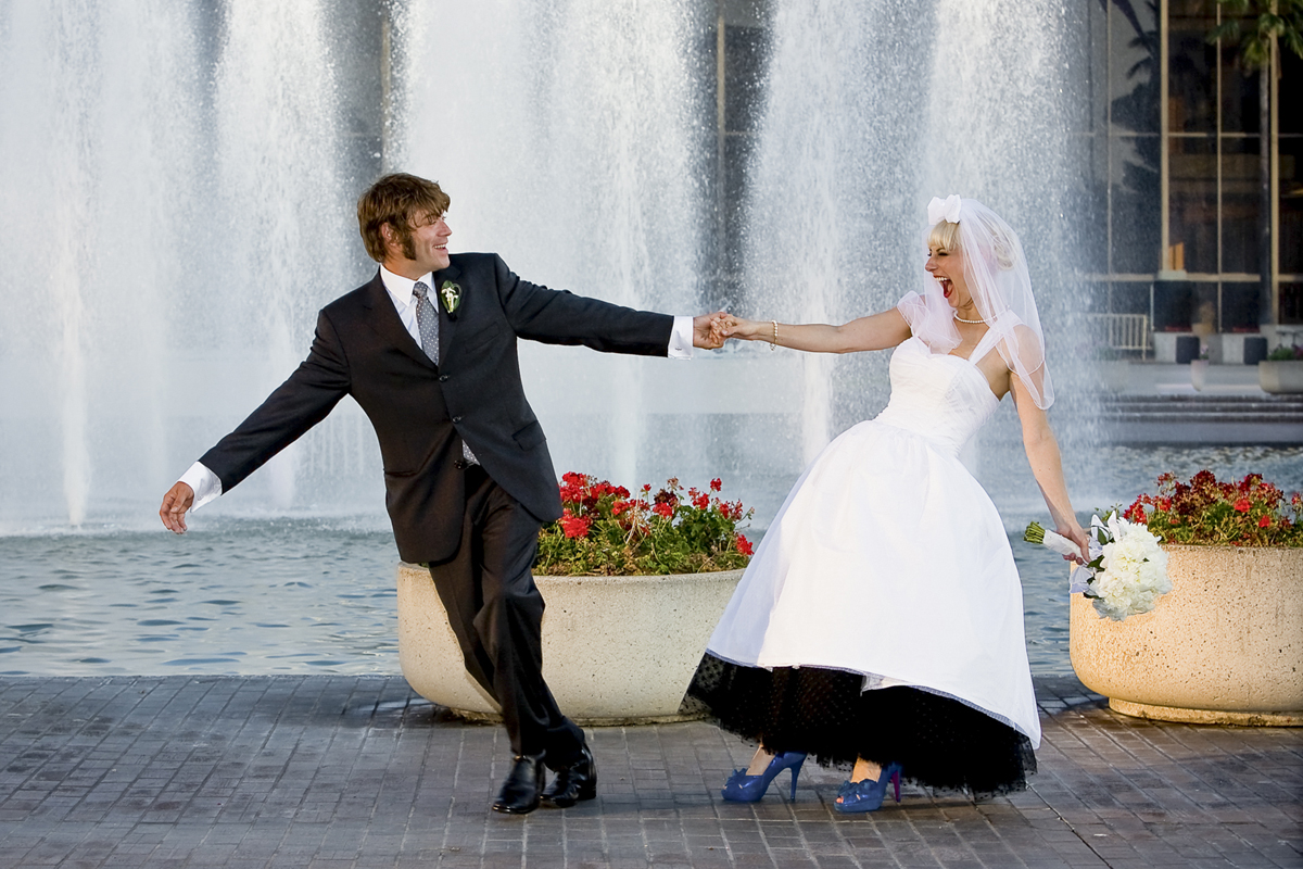 bride and groom pulling hands in front of fountains during a Los Angeles wedding, photographed beautifully