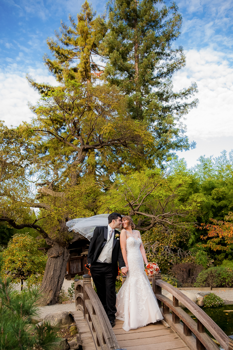 Bride and groom standing on garden bridge with veil blowing in the breeze at Hakone Gardens wedding san jose wedding photographer