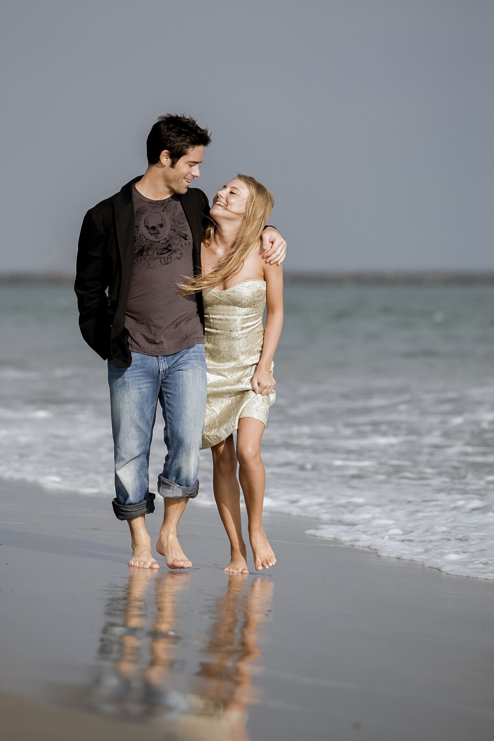 Couple walking along Baker Beach in San Francisco with ocean waves and Golden Gate Bridge in the background during a natural light engagement session