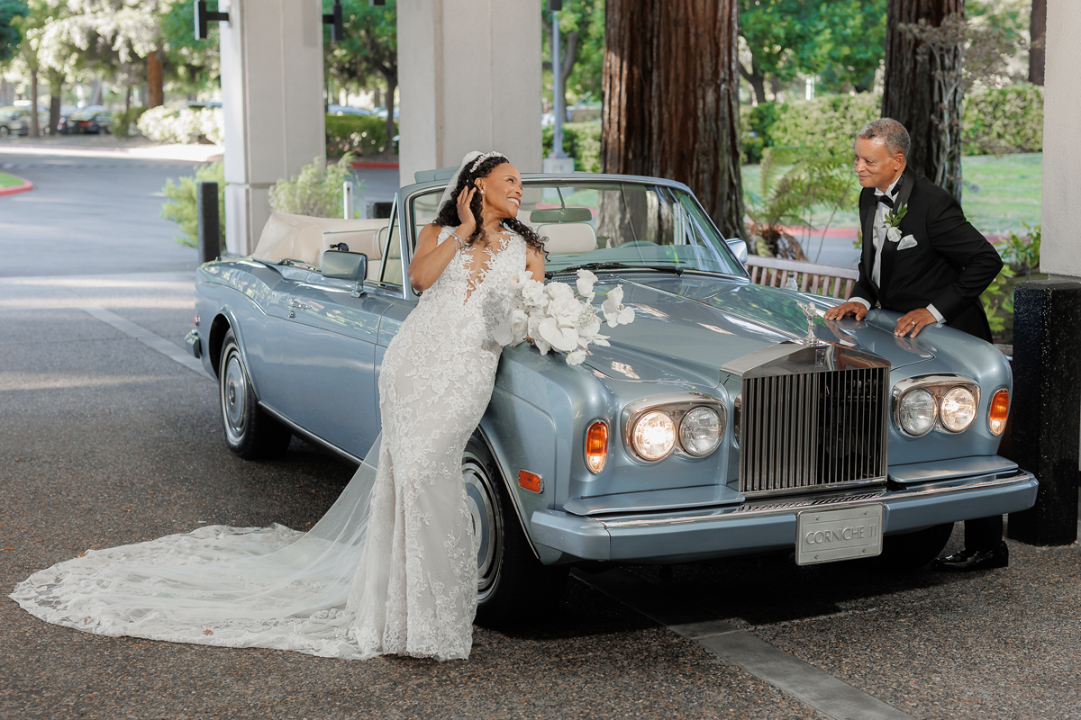 Fun-loving bride and groom posing with a classic car at San Ramon Marriott