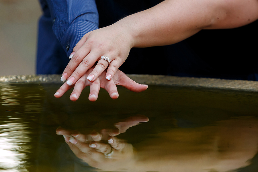 two hands holding as one showing engagement ring near fountain at uc davis arboretum in davis california