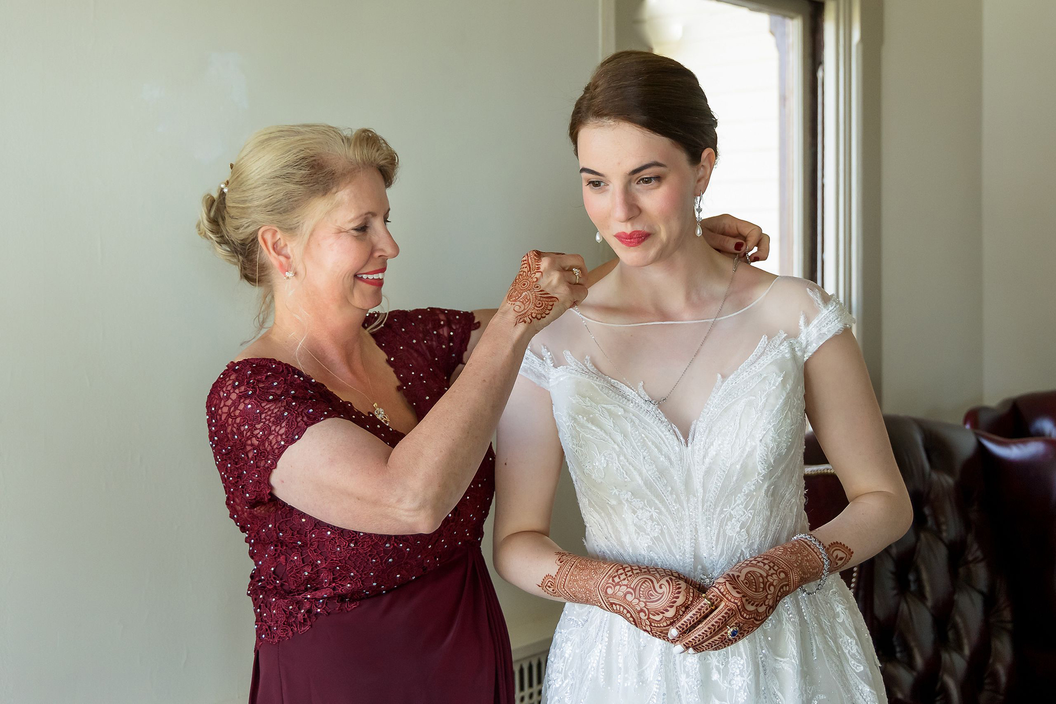 proud mother helping her daughter put on a necklace while getting ready for her wedding at The General's Residence in San Francisco, California