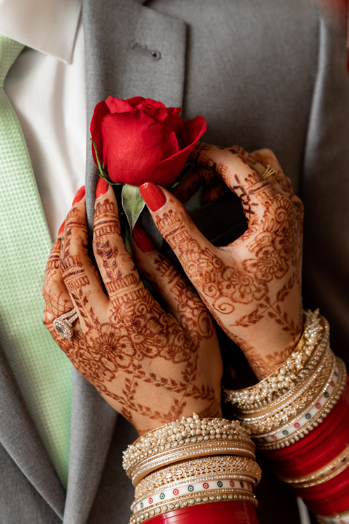 Close-up of henna decorated hands holding a groom’s boutonniere at The Walnut Hall in Yuba City during Indian wedding