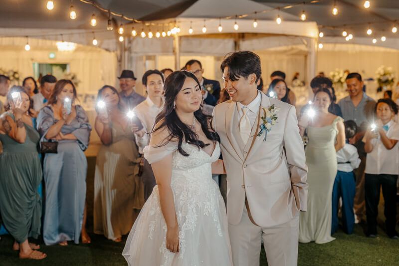 Bride and groom being serenaded by guests holding phone lights during their wedding reception at Grand Island Mansion